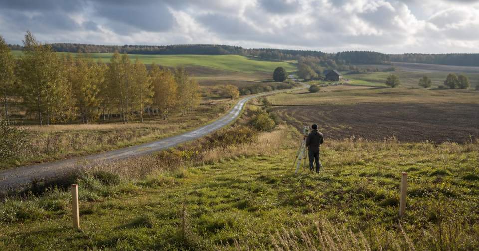 Surveyor assessing a rural Lithuanian plot beside its access road